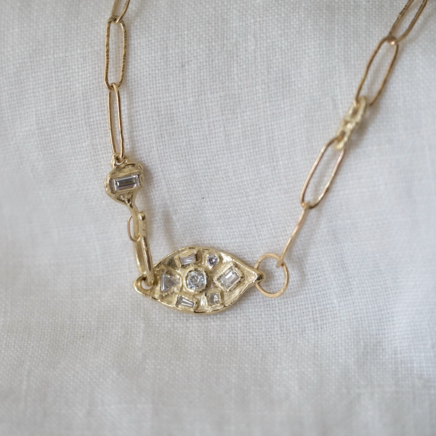 Gold necklace with eye-shaped pendant on a white fabric background