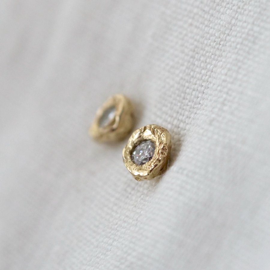 Gold earrings with a central gemstone on a white fabric background