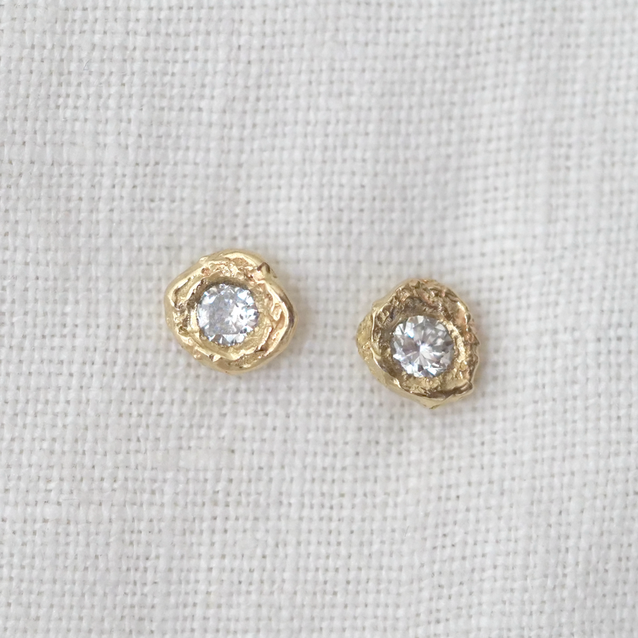 Gold earrings with clear gemstones on a light gray background