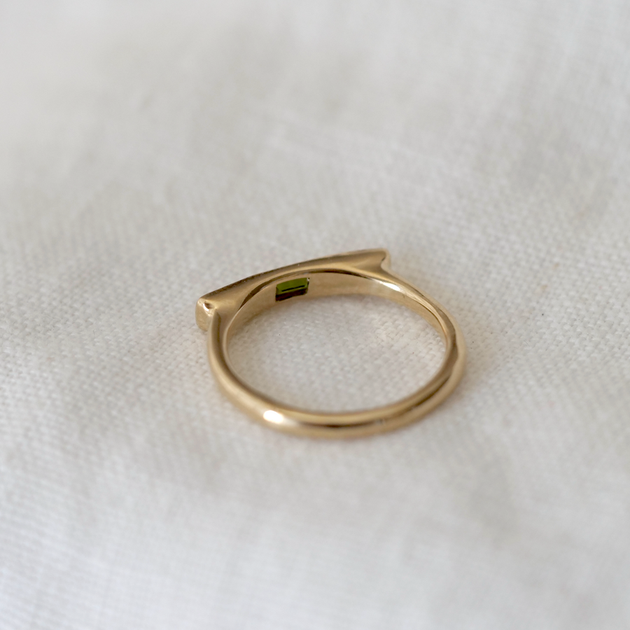 Gold ring with a green stone on a white fabric background