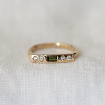 Gold ring with a green gemstone and diamonds on a white fabric background