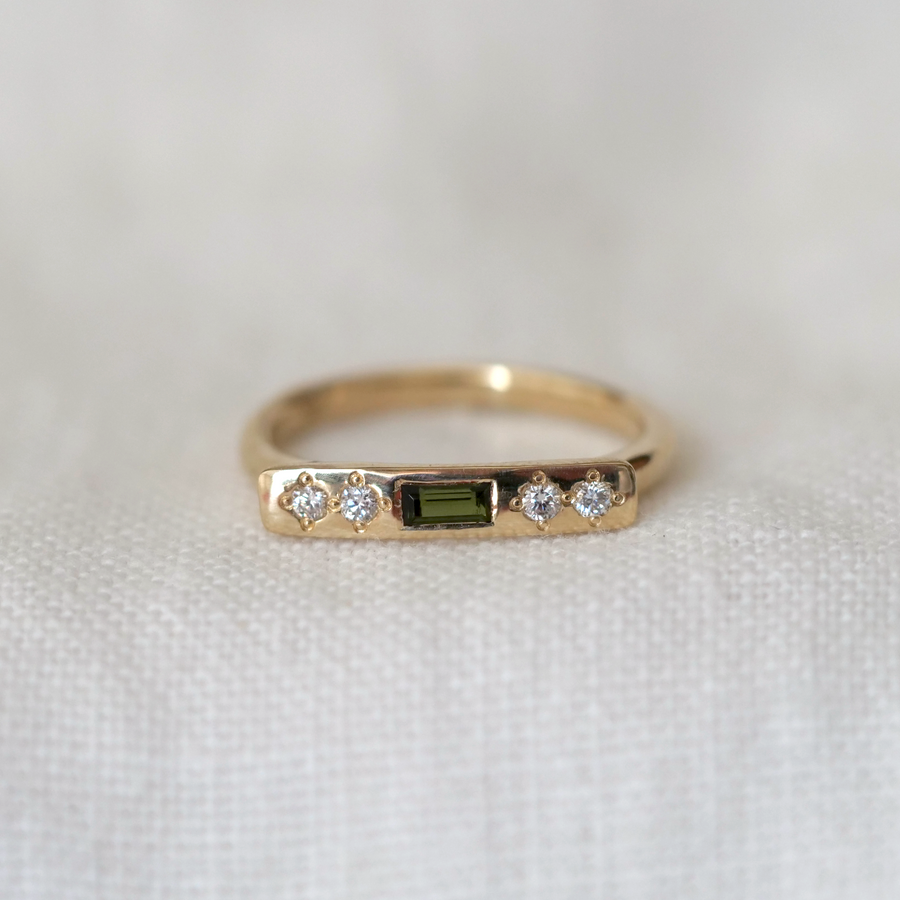 Gold ring with a green gemstone and diamonds on a white fabric background