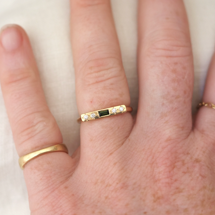Close-up of a hand wearing two gold rings with gemstones on a light background