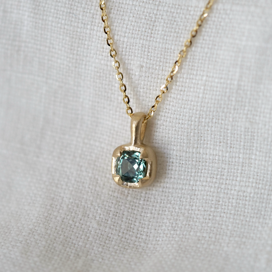 Gold necklace with a pendant featuring a blue gemstone on a white fabric background