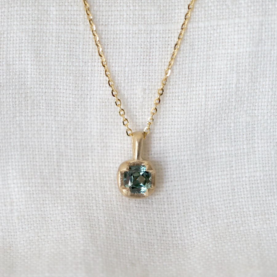 Gold necklace with a square green gemstone pendant on a white background