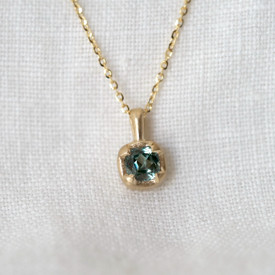 Gold necklace with a pendant featuring a green gemstone on a white background