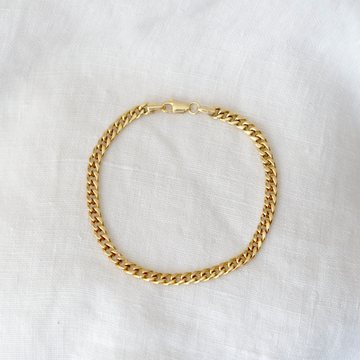 Gold curb chain bracelet on a white fabric background