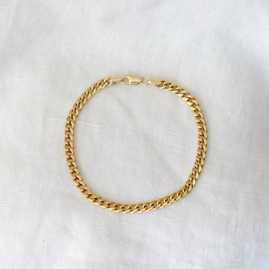 Gold curb chain bracelet on a white fabric background
