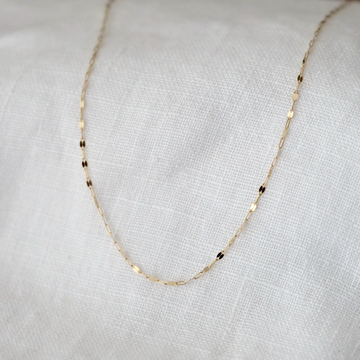 Gold chain necklace on a light gray fabric background