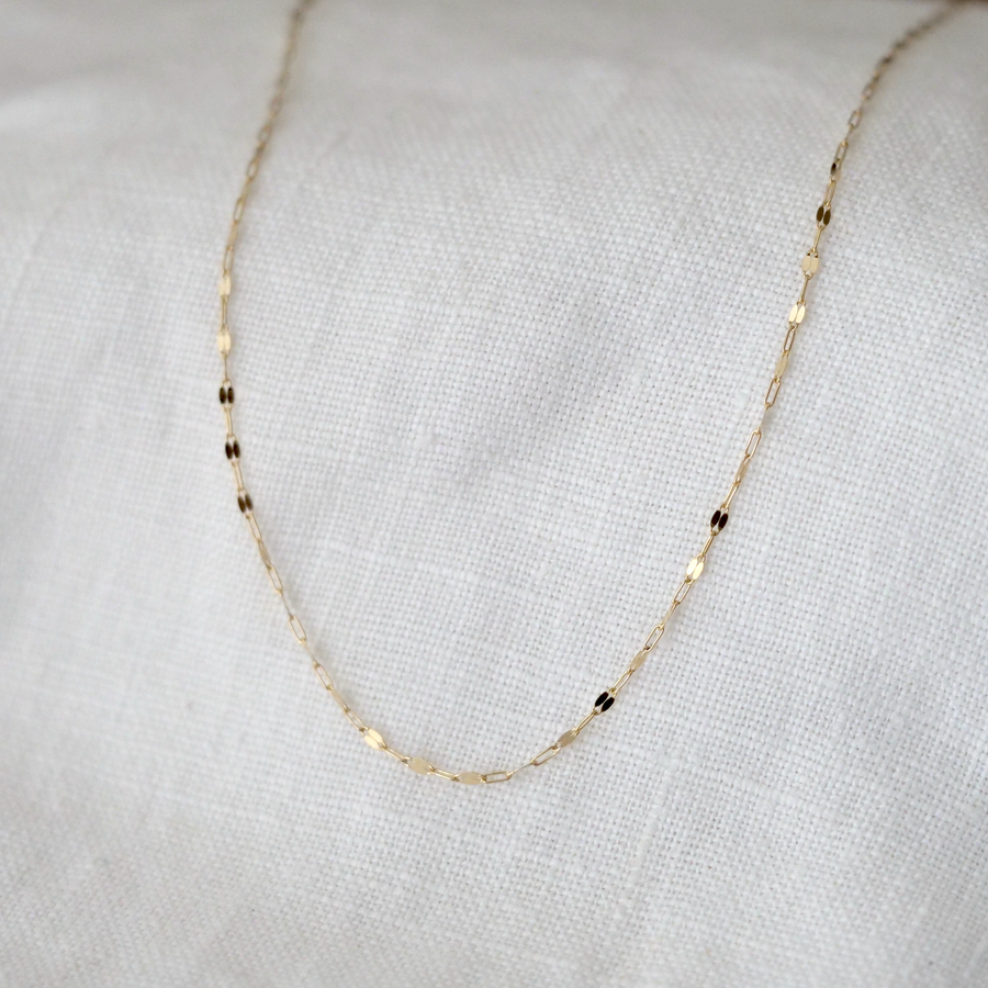 Gold chain necklace on a light gray fabric background