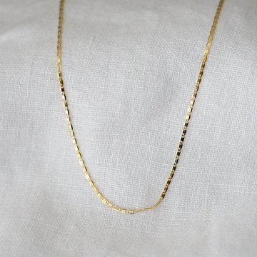 Gold shiny chain necklace on a light gray fabric background