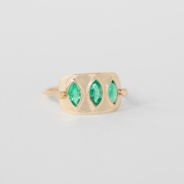 Gold ring with three marquise cut green emerald stones on a light gray background