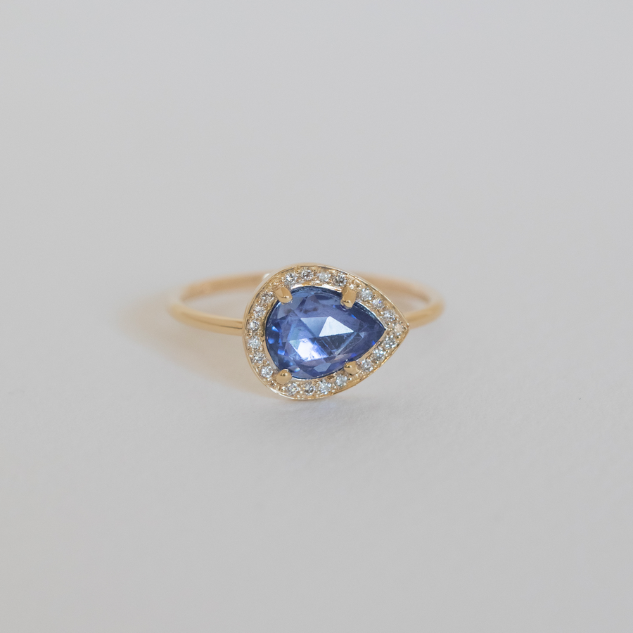 Gold ring with a blue gemstone and diamond accents on a light gray background