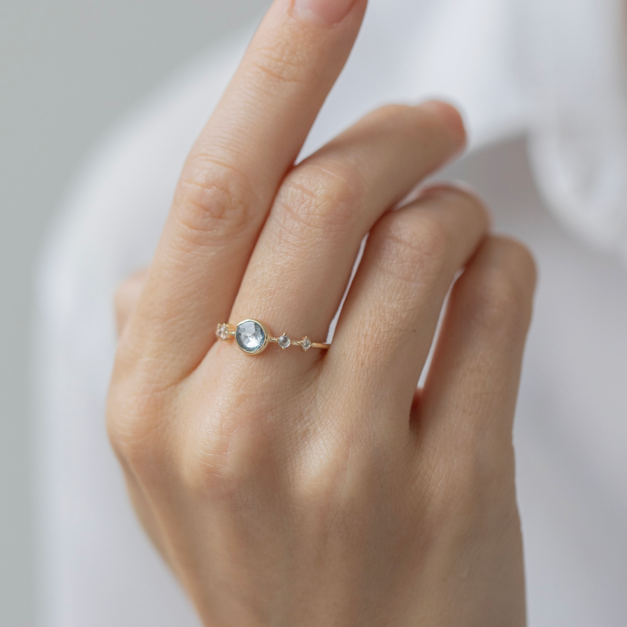Hand wearing a delicate gold ring with a gemstone on a neutral background