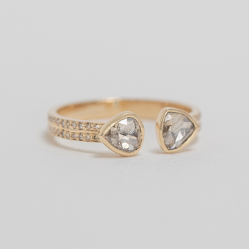 Gold ring with two teardrop-shaped diamond stones on a light gray background