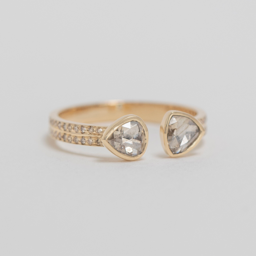 Gold ring with two teardrop-shaped diamond stones on a light gray background