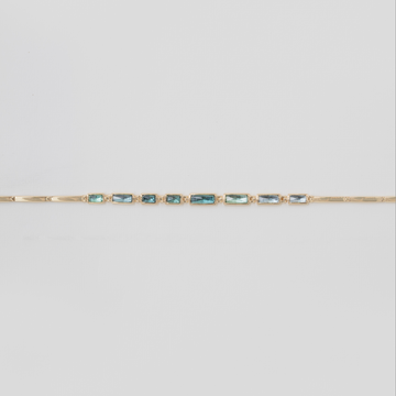 Gold bracelet with blue gemstones on a light gray background