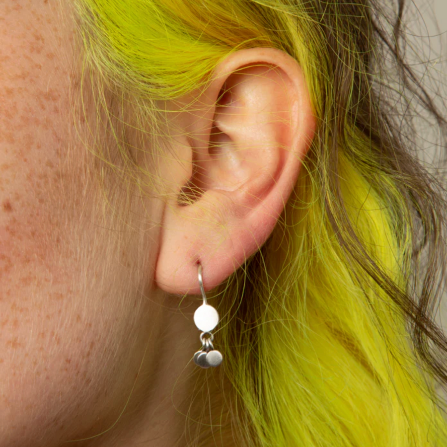 Close-up of an ear with a silver earring against a neutral background