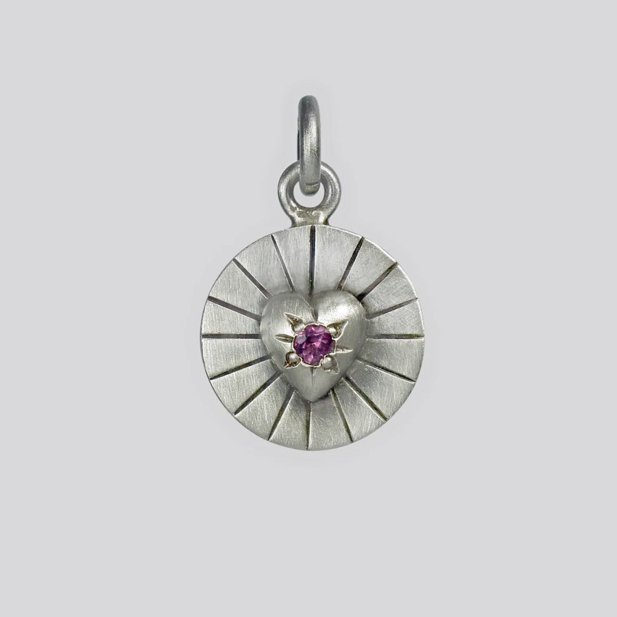 Silver pendant with a heart design and purple gemstone on a light gray background
