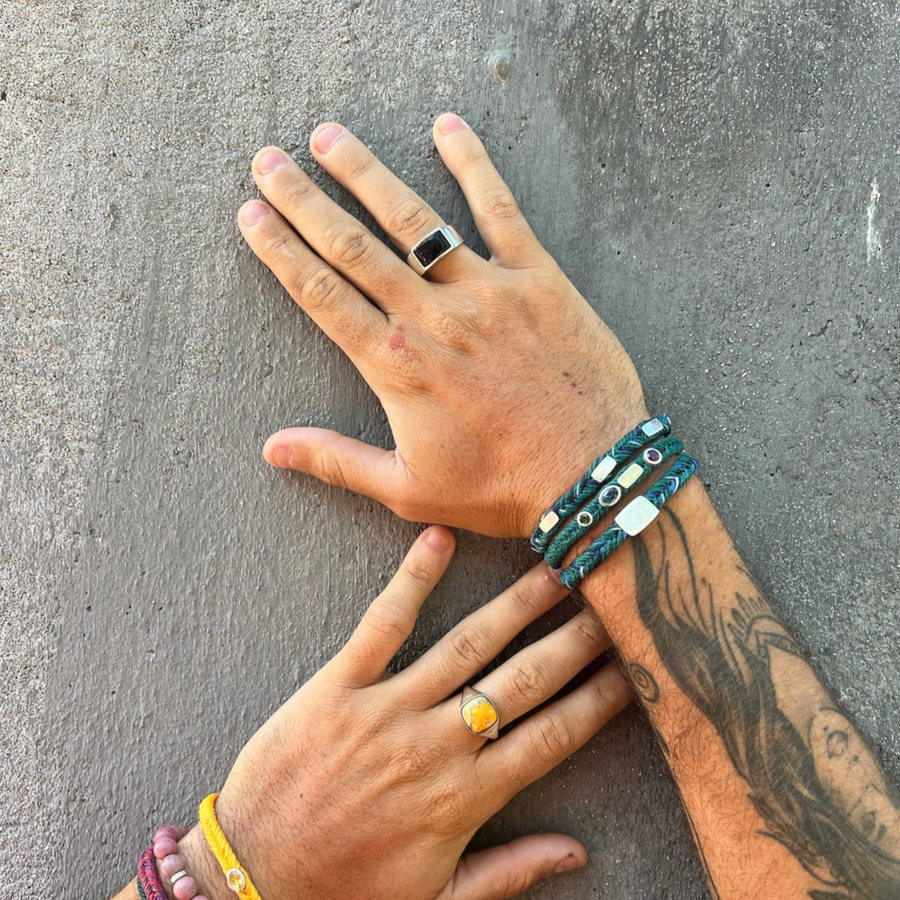 Two hands with rings and bracelets on a textured gray surface