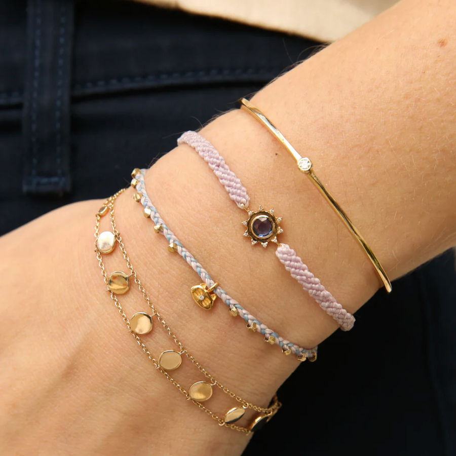 Close-up of a wrist wearing multiple gold and beaded bracelets against a dark background