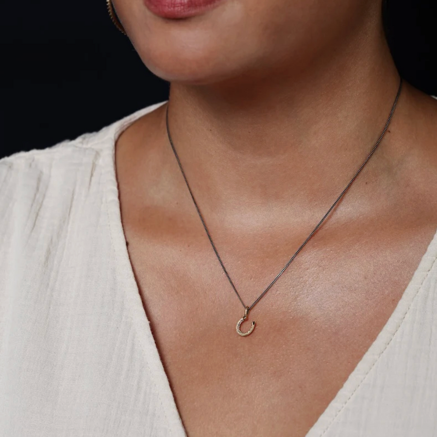 Necklace with a small pendant worn by a person in a white top against a dark background