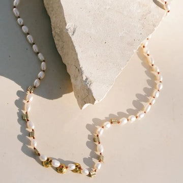 Freshwater pearls delicately line the base of the neck. Knotted in place, the pearls are interwoven with brass bars and blossoms