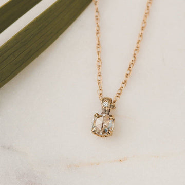 A sparkling rose cut moissanite is carefully set in solid gold with a twinkling diamond accent. 