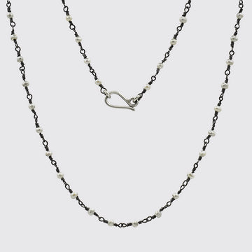 Two layered necklaces with black chain and white beads on a light gray background