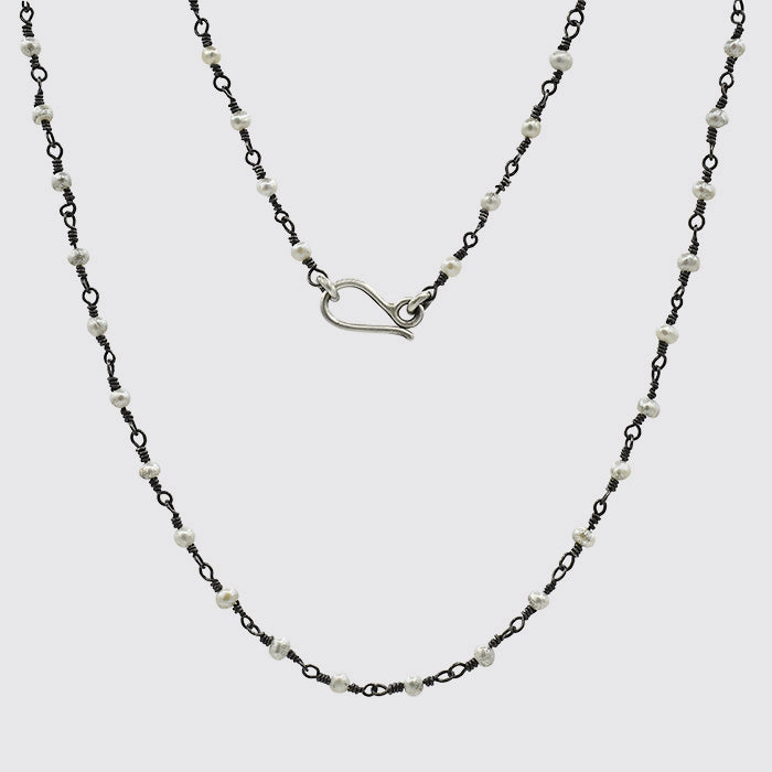 Two layered necklaces with black chain and white beads on a light gray background