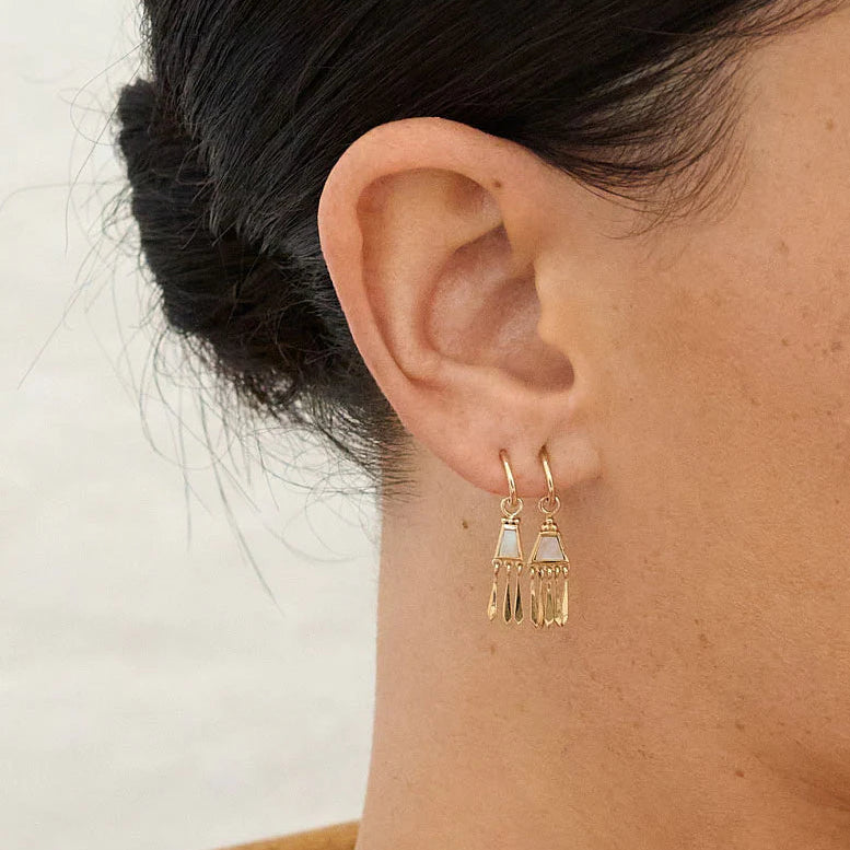 Gold earrings worn by a person with a neutral background
