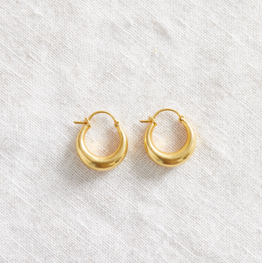 Hollow 18k Indian gold hoops on white linen backdrop